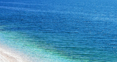 Feiner Kiesestrand im Hintergrund das azurblaue Meer.